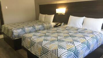 Habitación de hotel con dos camas, cada una con ropa de cama estampada, una mesita de noche con lámpara y teléfono.