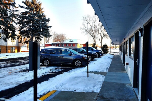 A parking area with cars and a building with a covered walkway.
