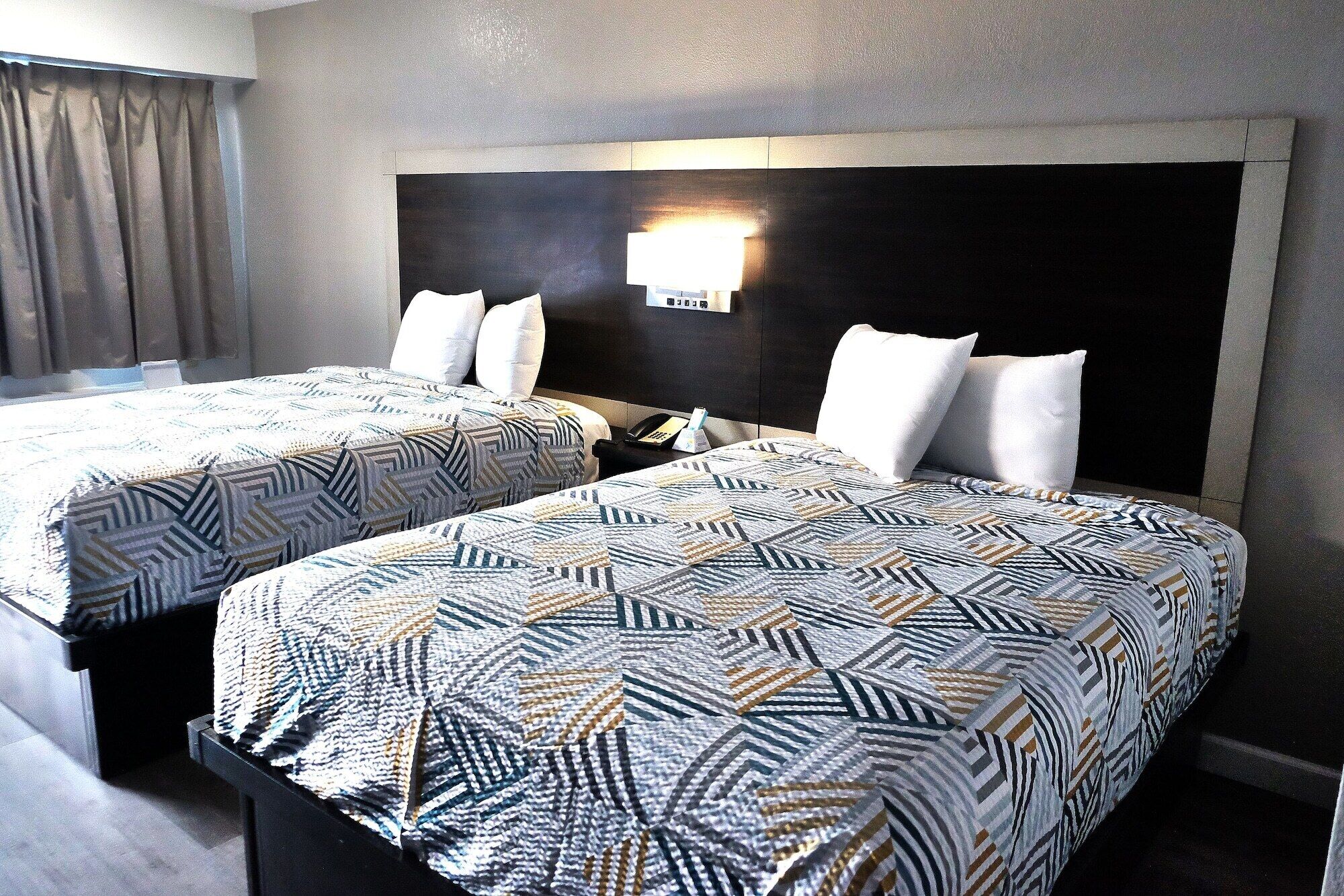 A hotel room with two beds, a nightstand, a lamp, and a wall-mounted phone.