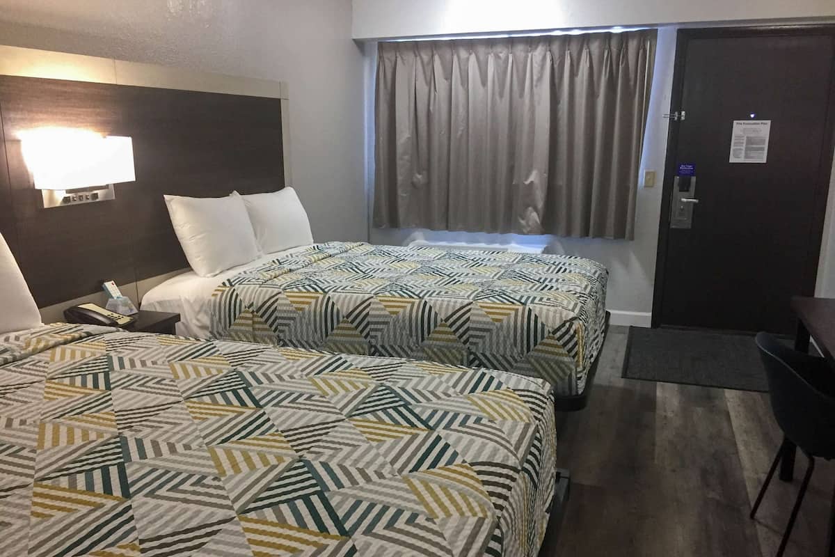 A hotel room with two beds, a nightstand, a desk, and a door with a fire evacuation plan.