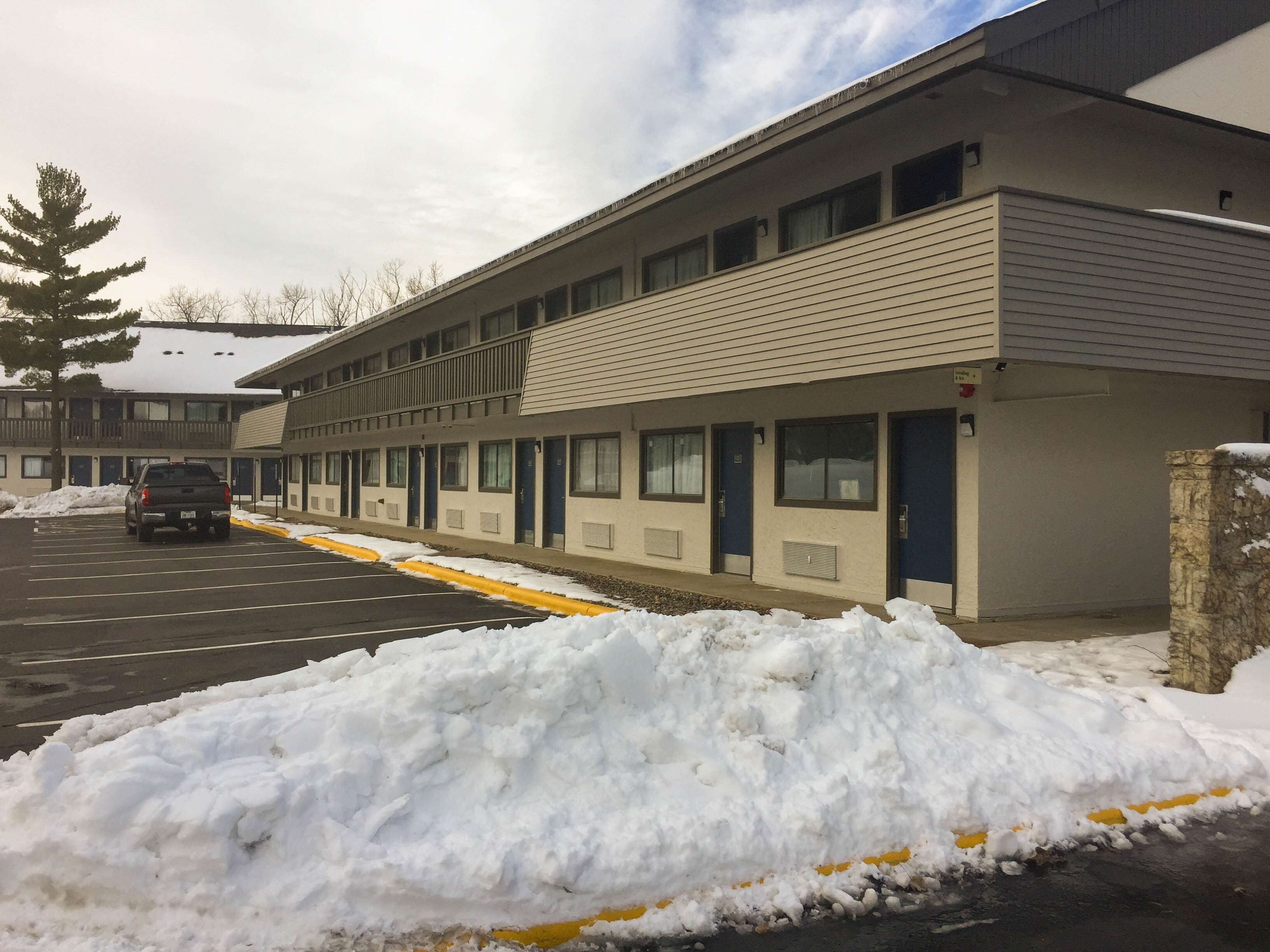 A motel with a row of rooms, a parking lot, and a snow-covered ground.