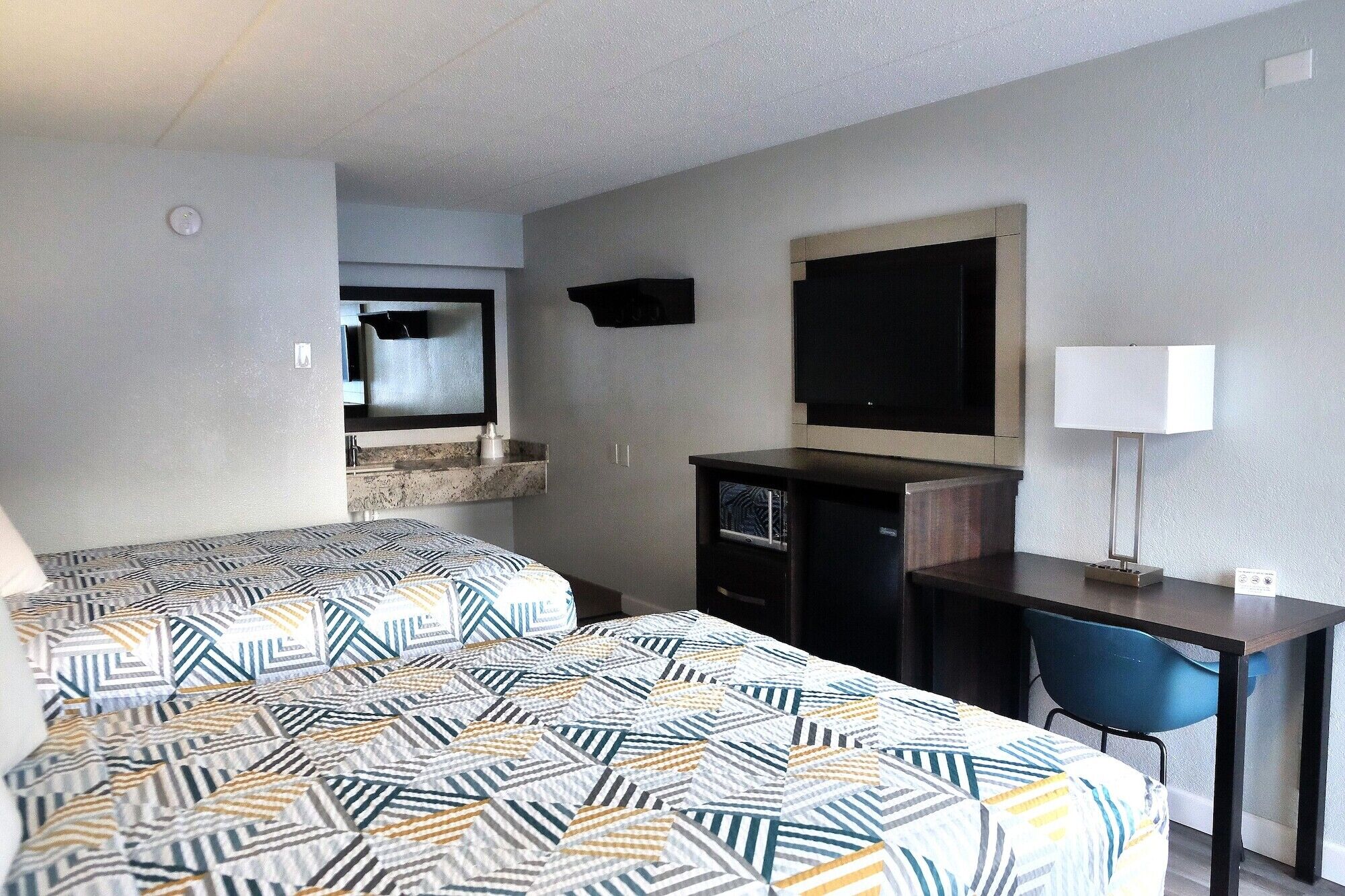 Quarto de hotel com duas camas, uma escrivaninha, uma cadeira, uma televisão e um abajur.
