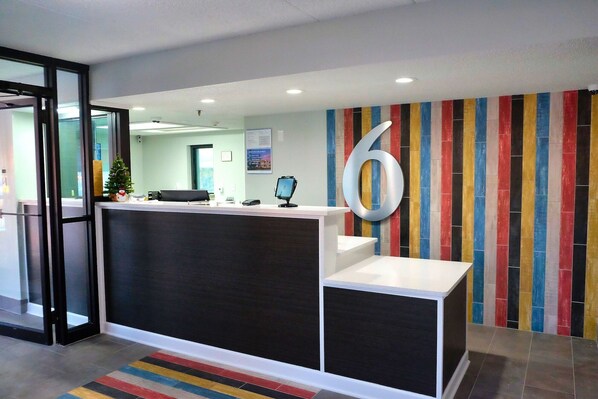 A reception area with a modern design, featuring a large number '6' on the wall, a reception desk, and a colorful striped wall. - Motel 6 Burnsville, MN (Burnsville)