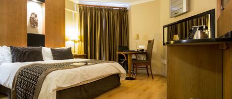 A hotel room with a bed, desk, chair, and a small kitchenette area.
