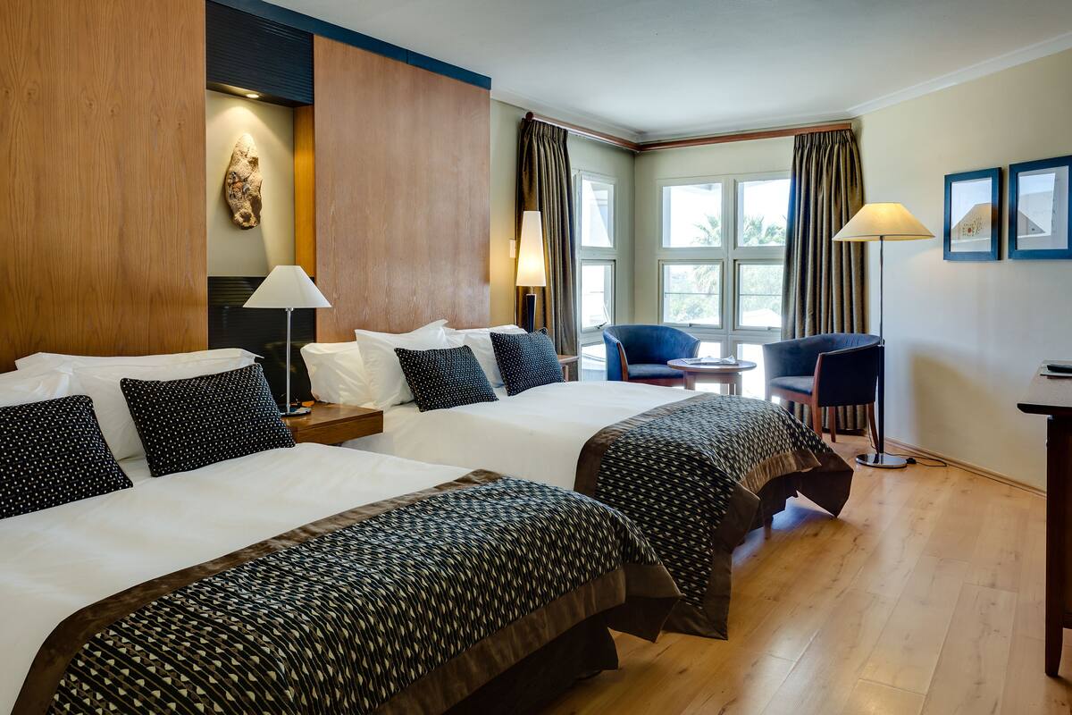 A hotel room with two beds, a desk, a chair, and a lamp.