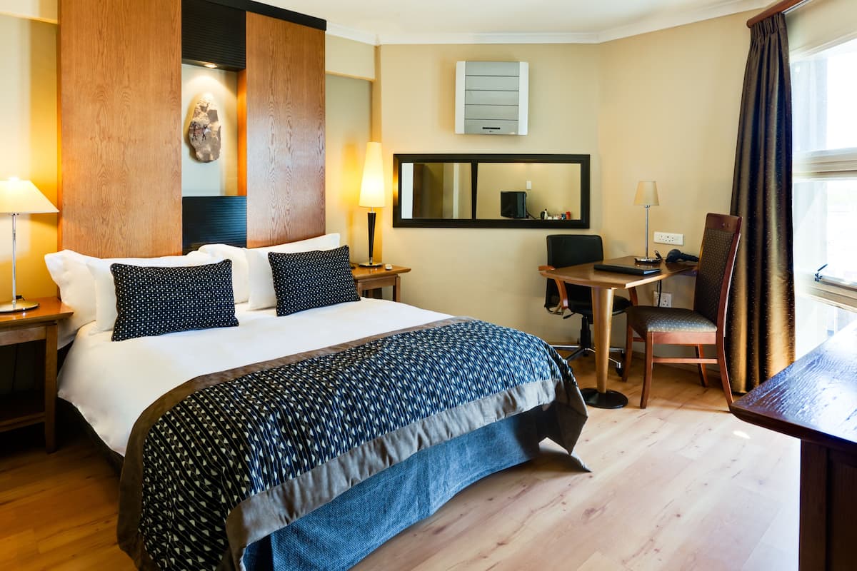 A hotel room with a large bed, a desk, a chair, and a mirror.