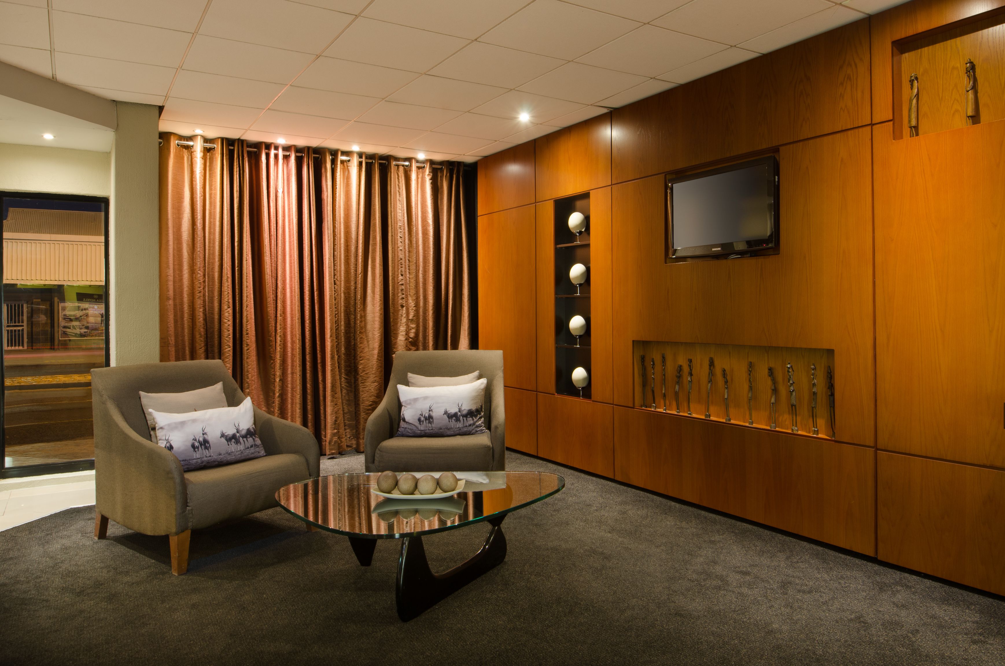 A modern room with two armchairs, a glass coffee table, a flat-screen TV, and a wooden cabinet with decorative items.