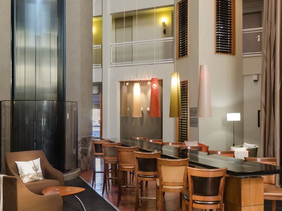 A hotel lobby with a central seating area, a glass elevator, and a multi-level balcony with railings.