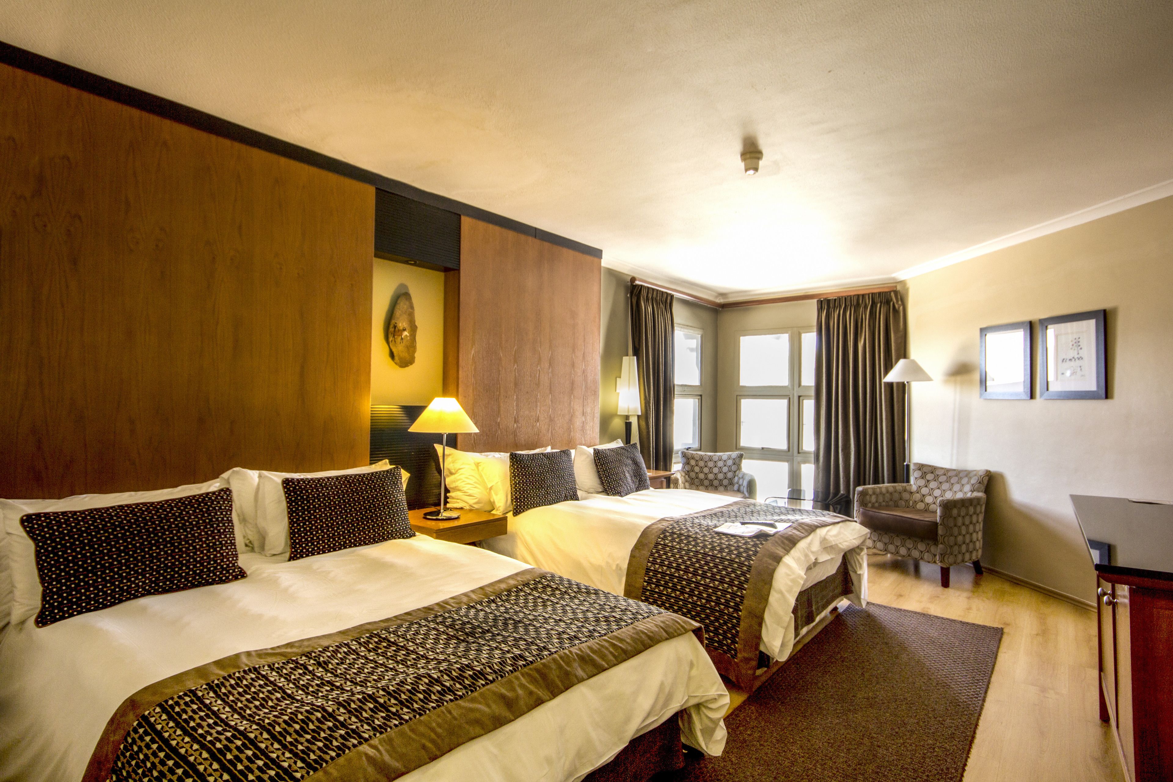 Camera d'albergo con due letti, una scrivania, una sedia e un'ampia finestra.