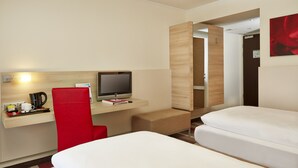 A hotel room with a bed, a desk with a computer, a red chair, and a small seating area. - Sunday Hotel Bad Soden (Bad Soden am Taunus)