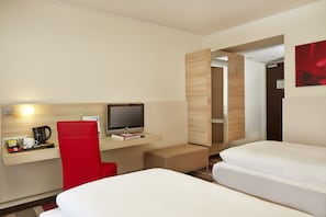 Habitación de hotel con cama, escritorio con computadora, una silla roja y un pequeño rincón de descanso.