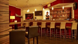 A bar area with multiple stools, a bartender, and a well-stocked liquor shelf. - Sunday Hotel Bad Soden (Bad Soden am Taunus)