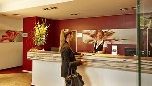 A reception area with a marble counter, a receptionist, and a large floral decoration. - Sunday Hotel Bad Soden (Bad Soden am Taunus)