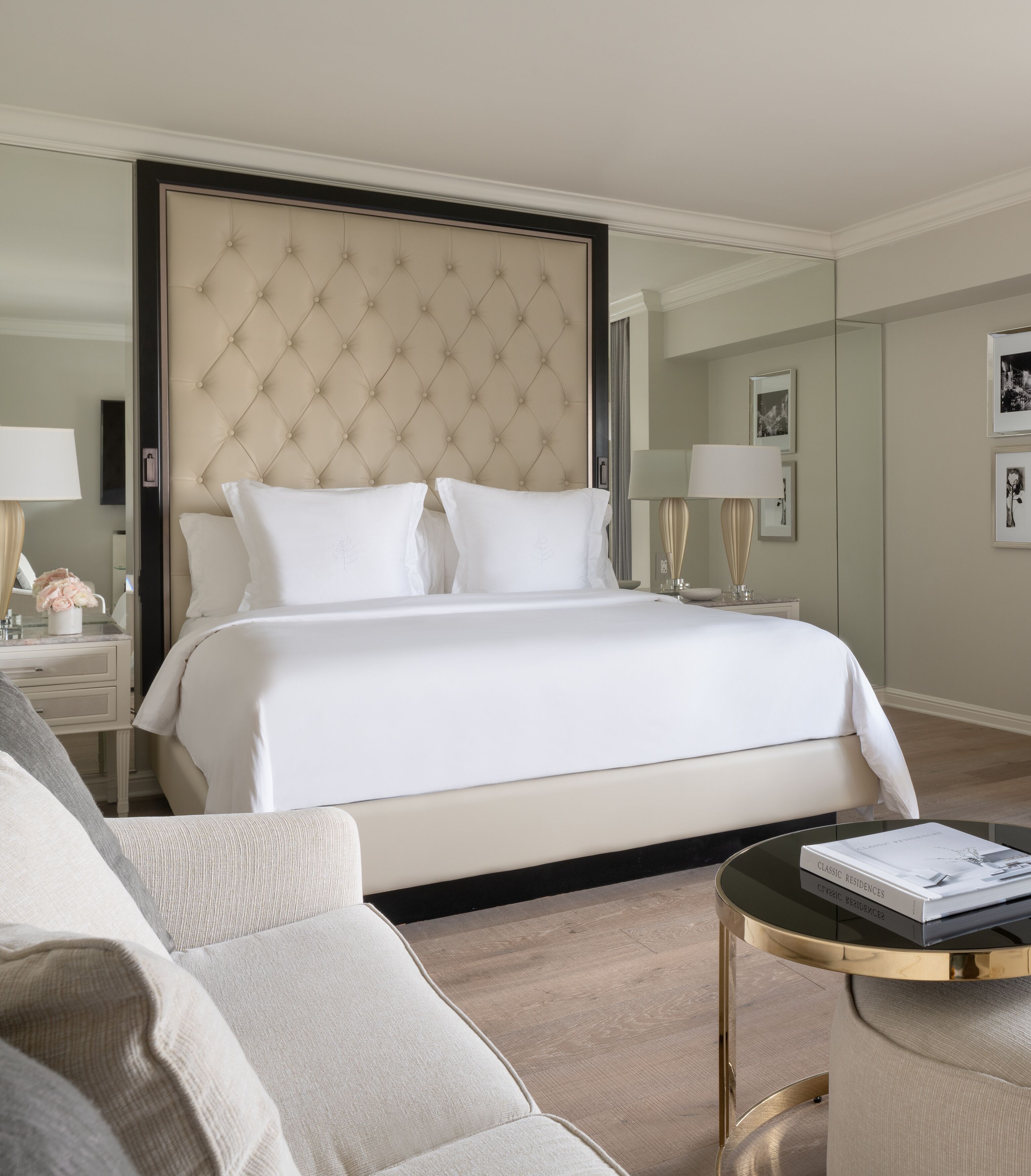 Una habitación de hotel moderna con una cama grande, una mesita de noche con lámpara, una mesa de centro redonda y un sofá.