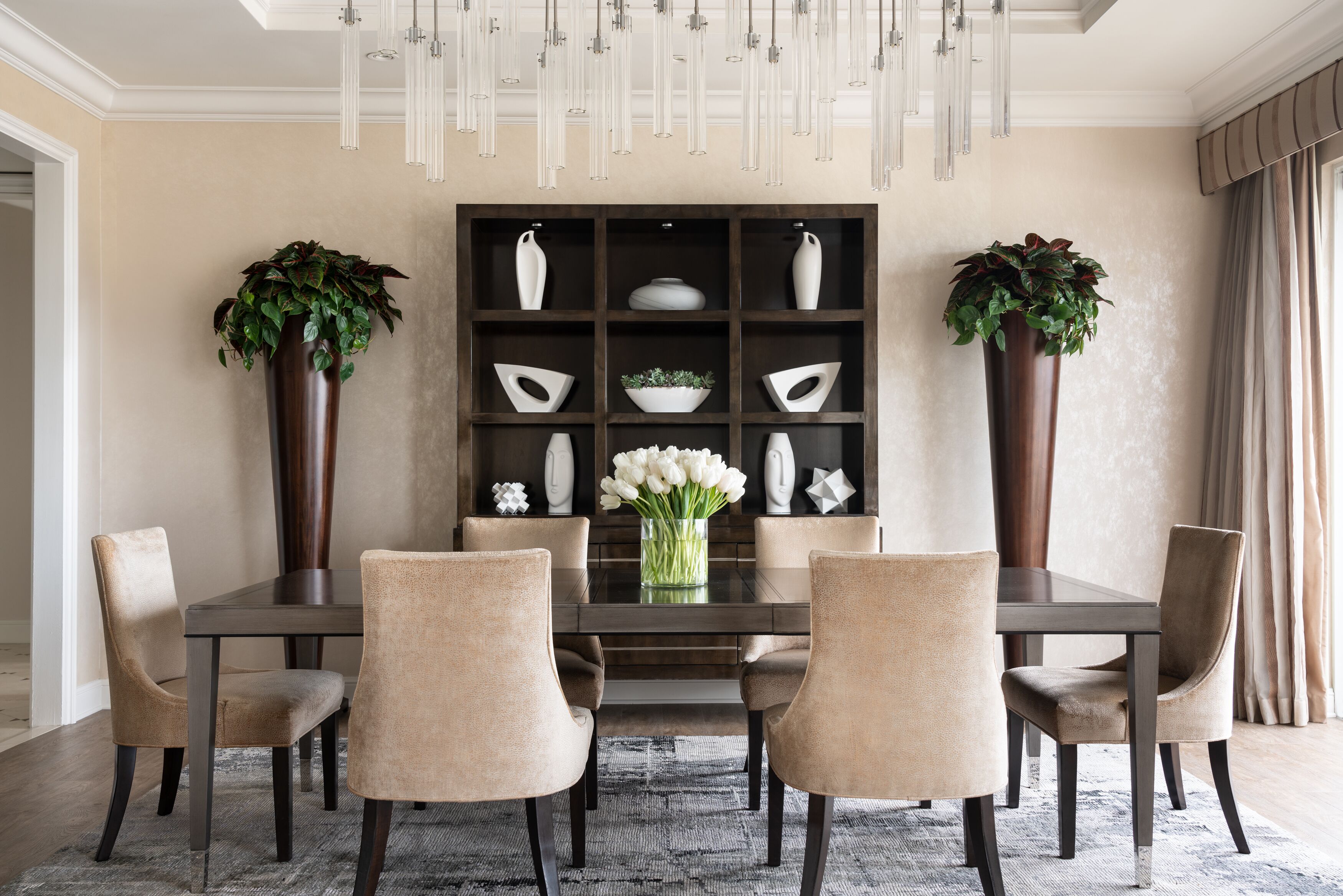 Comedor con una mesa rectangular, seis sillas, un florero y una estantería decorativa con jarrones y plantas.