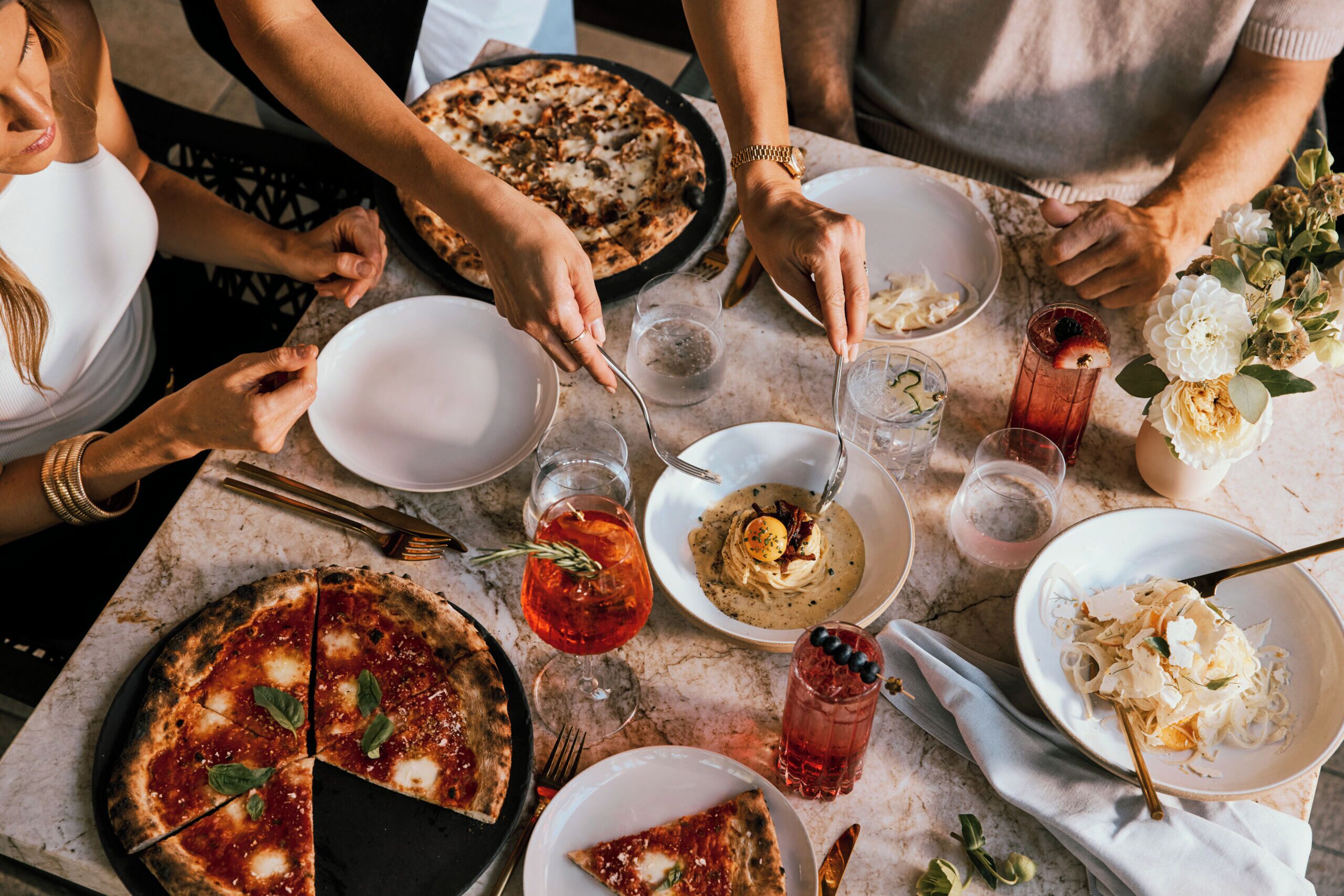 A group of people around a table with a pizza, drinks, and various dishes.