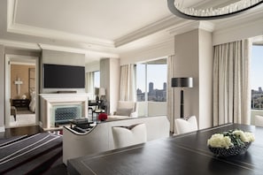 A modern hotel room with a dining area, a fireplace, a flat-screen TV, and a city view.