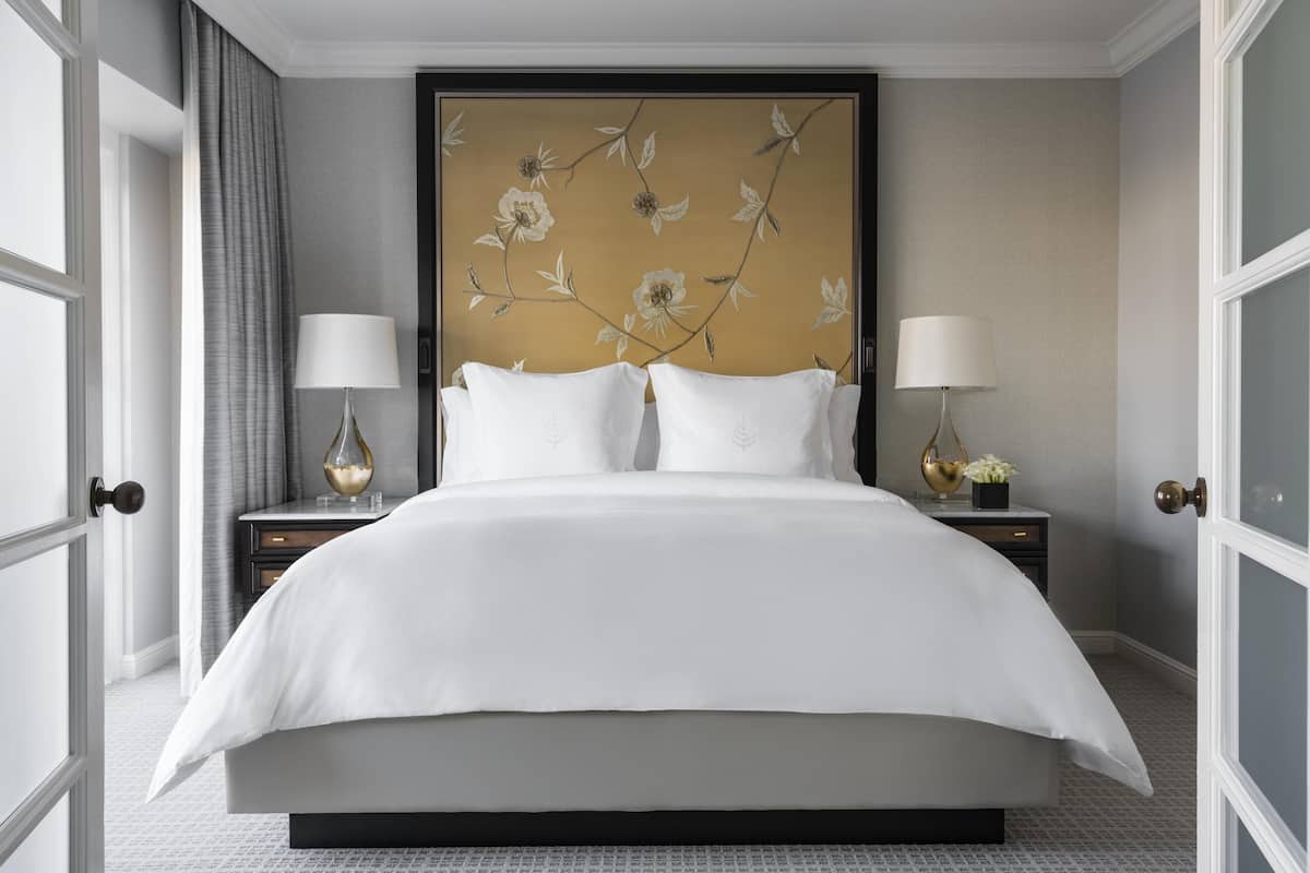 A large bed with white linens, two bedside tables with lamps, and a floral wall mural.