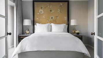 A large bed with white linens, two bedside tables with lamps, and a floral wall mural.