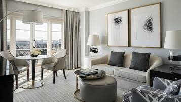 Ett modernt hotellrum med ett runt matbord, två soffor, ett soffbord och ett stort fönster med utsikt över staden.
