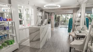 A modern spa with a marble reception desk, glass display cases, and a view of the garden.
