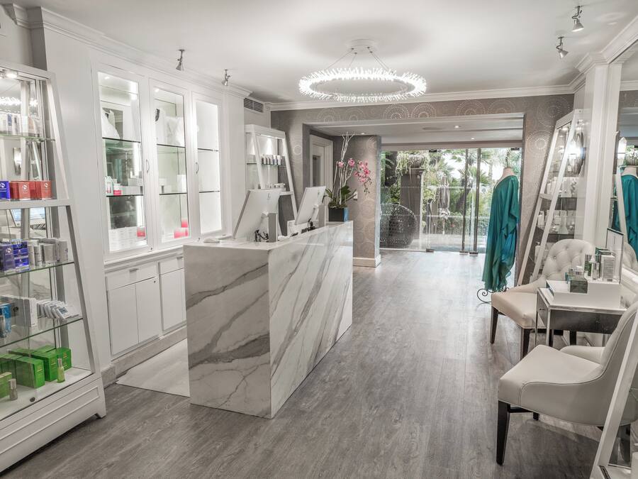 A modern spa with a marble reception desk, glass display cases, and a view of the garden.
