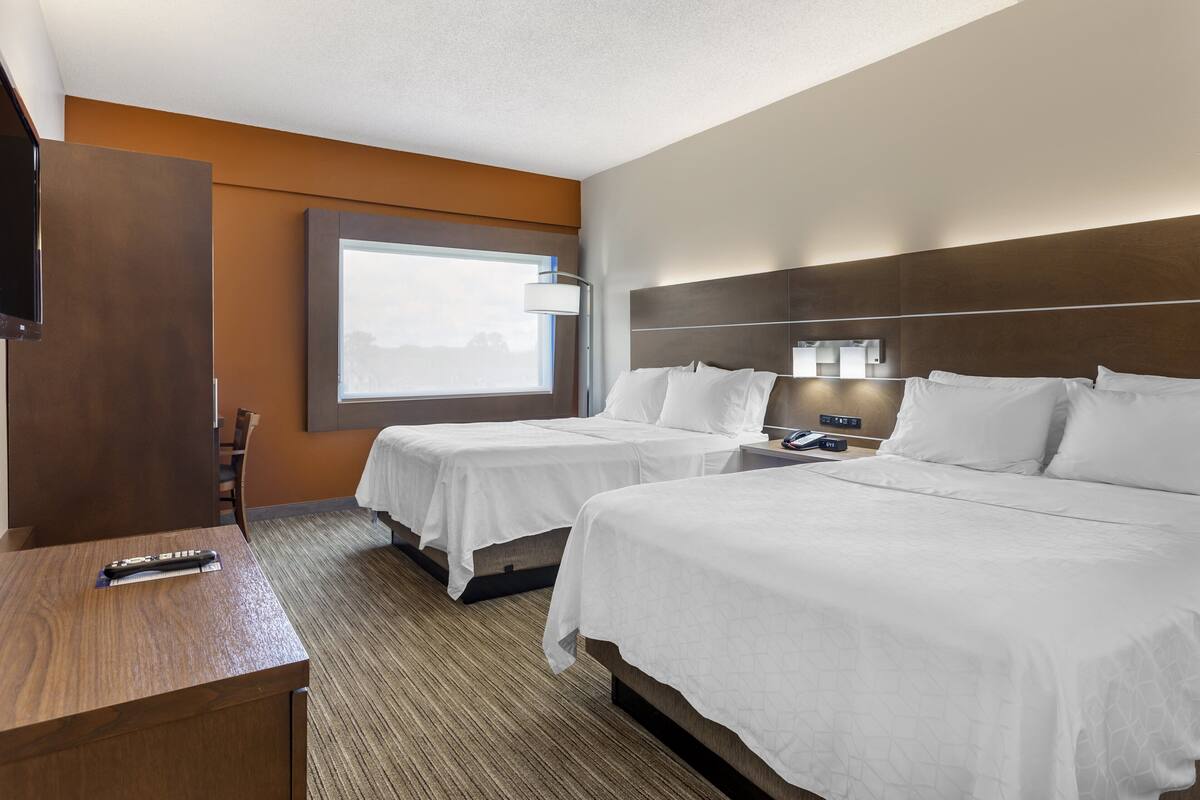 Quarto de hotel com duas camas, uma escrivaninha, uma televisão e uma janela com vista.