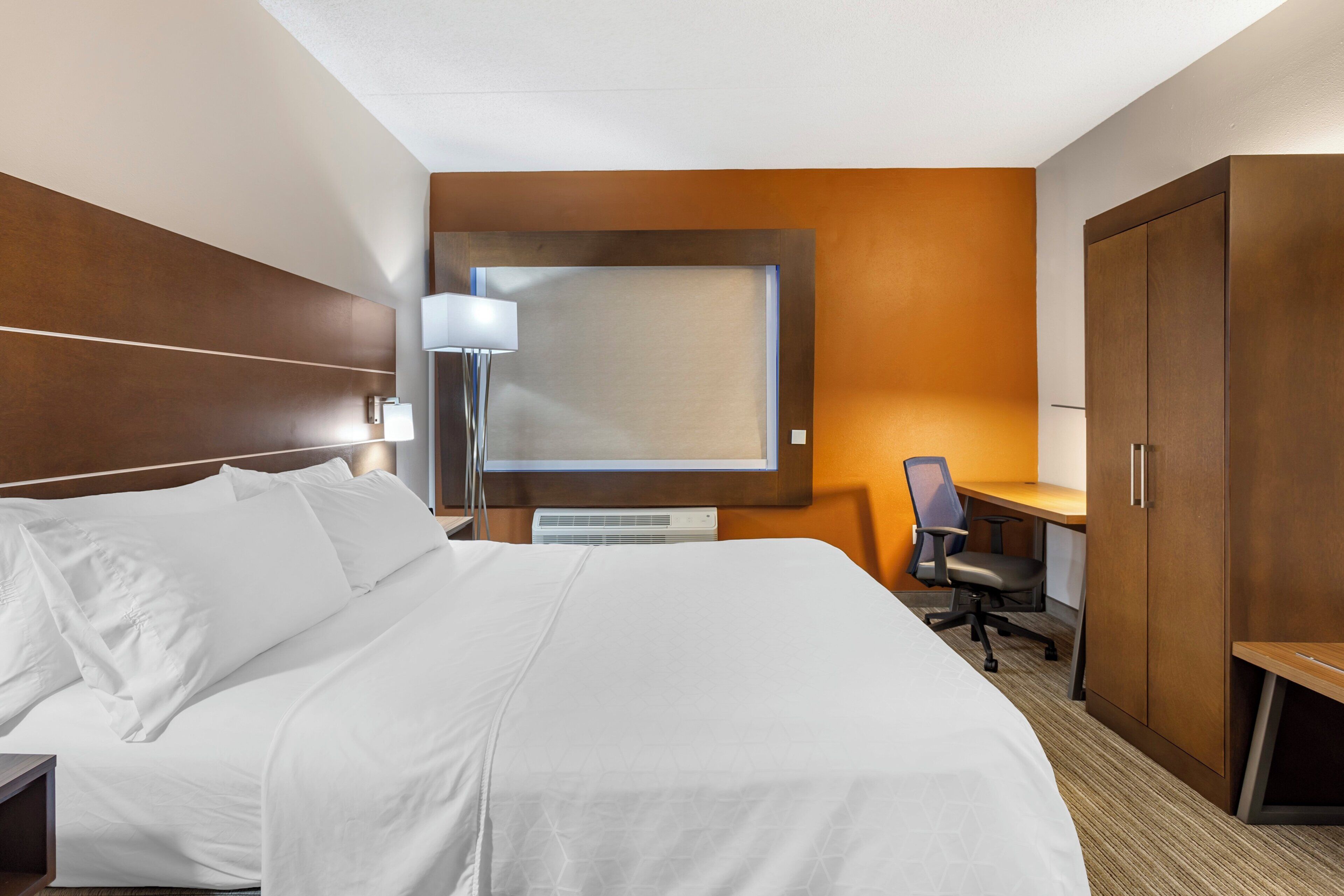 A hotel room with a large bed, a desk, a chair, a wardrobe, and a wall-mounted TV.