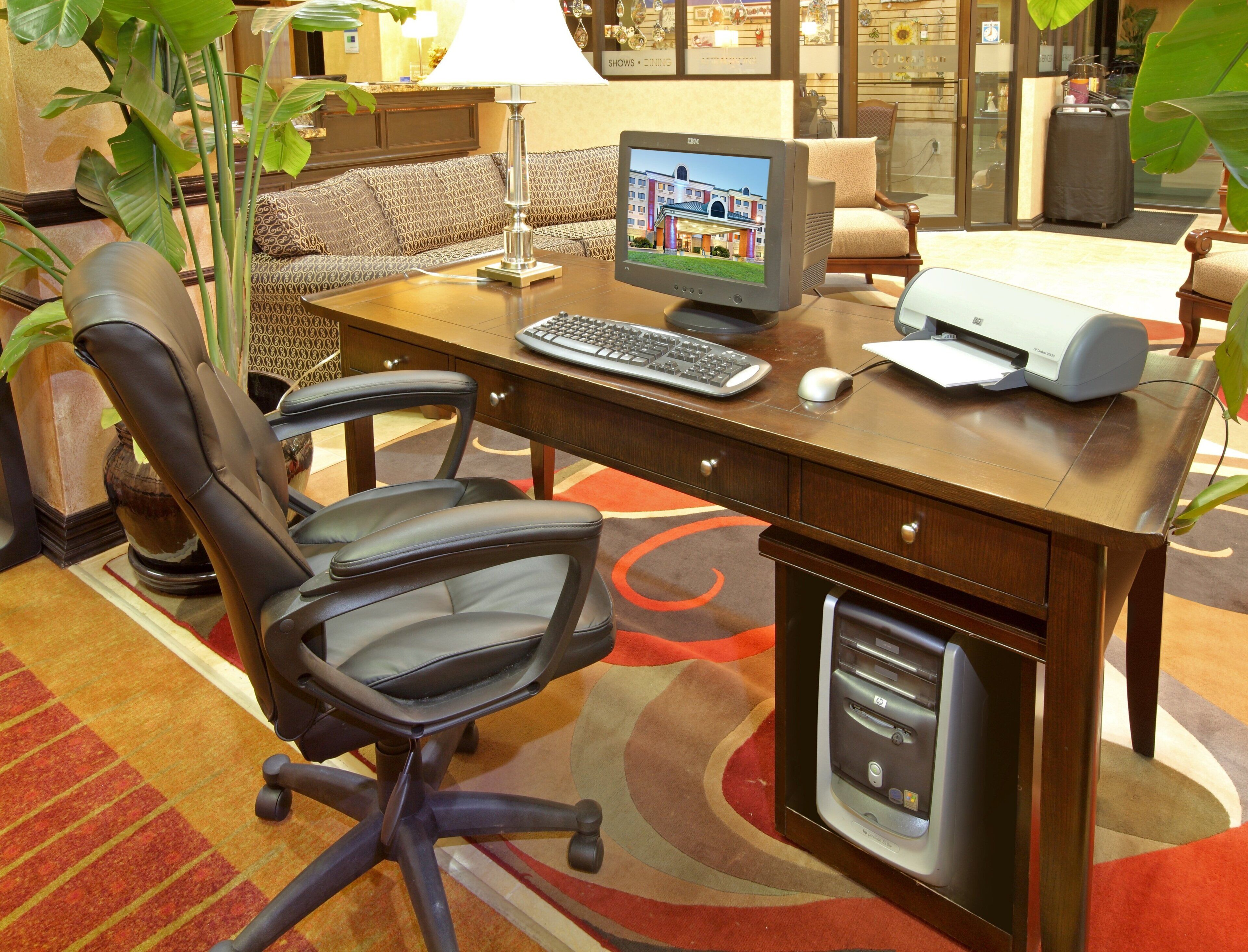 A hotel room with a desk, computer, chair, lamp, and a large window.