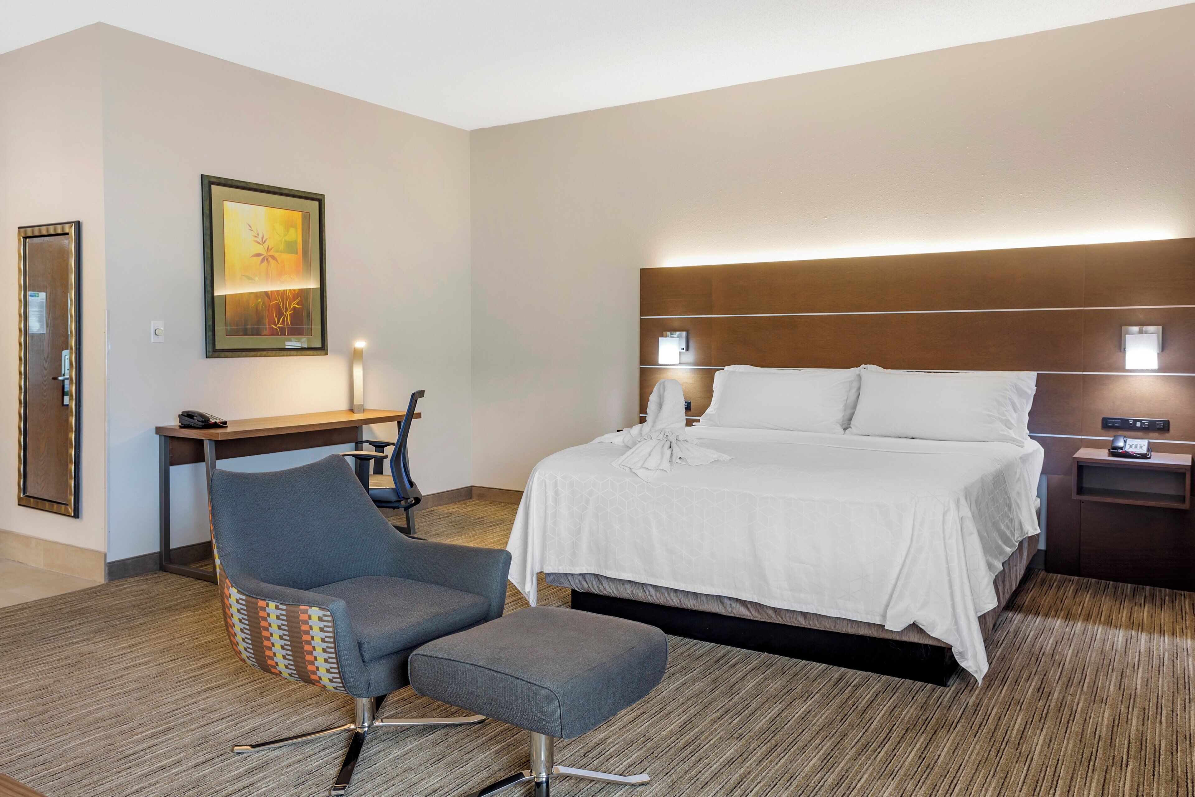 A hotel room with a bed, a desk, a chair, and a painting on the wall.
