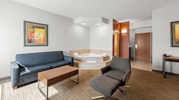 Habitación de hotel moderna con sofá, sillón y una mesita. Hay una bañera en la esquina y una puerta que conduce a otra habitación.