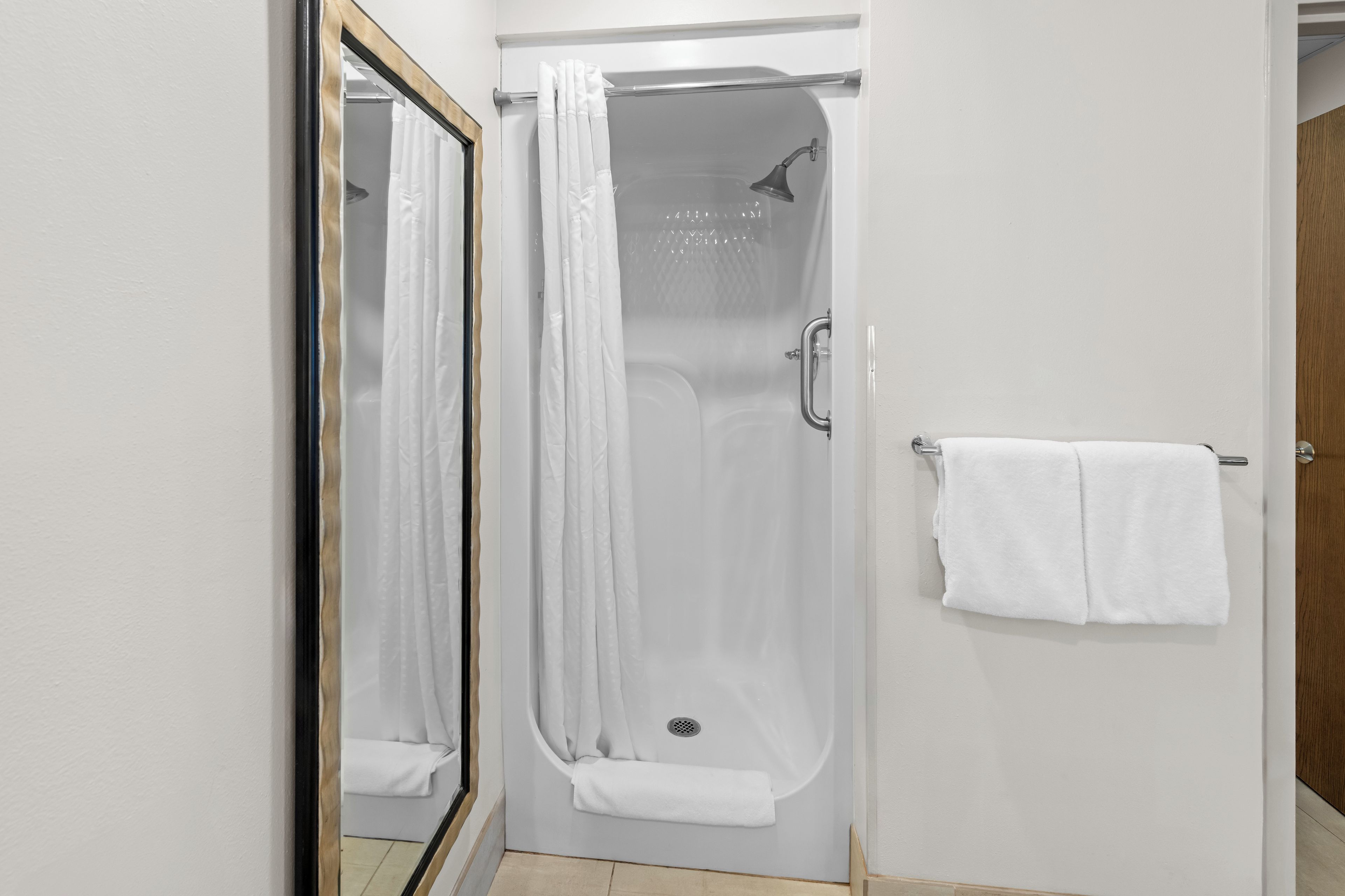 A bathroom with a shower, a towel rack, and a mirror.