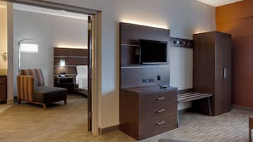 Habitación de hotel con cama, escritorio, televisor, armario y baño visible a través de una puerta abierta.
