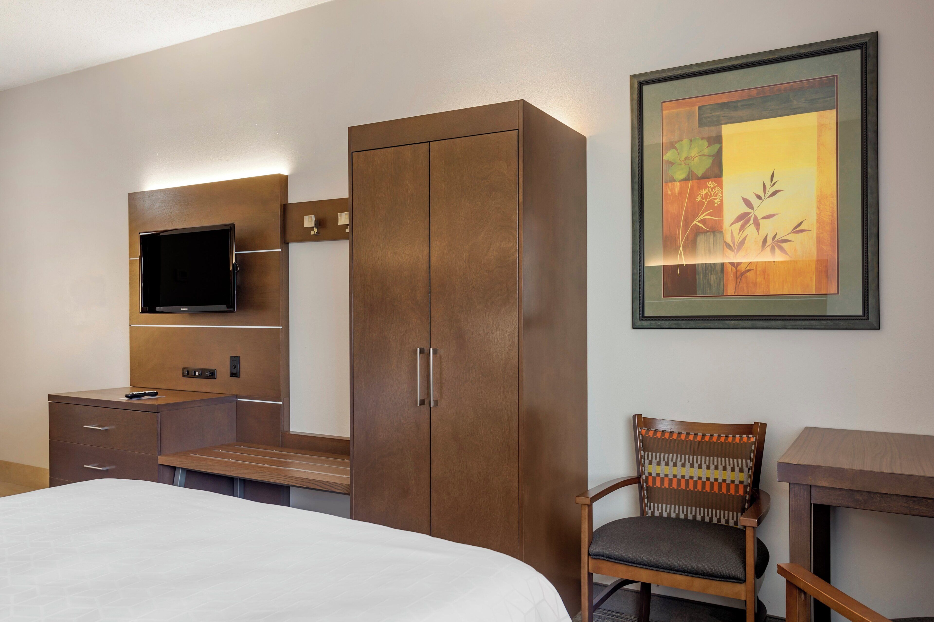 A hotel room with a bed, a television, a wardrobe, a chair, and a framed picture on the wall.