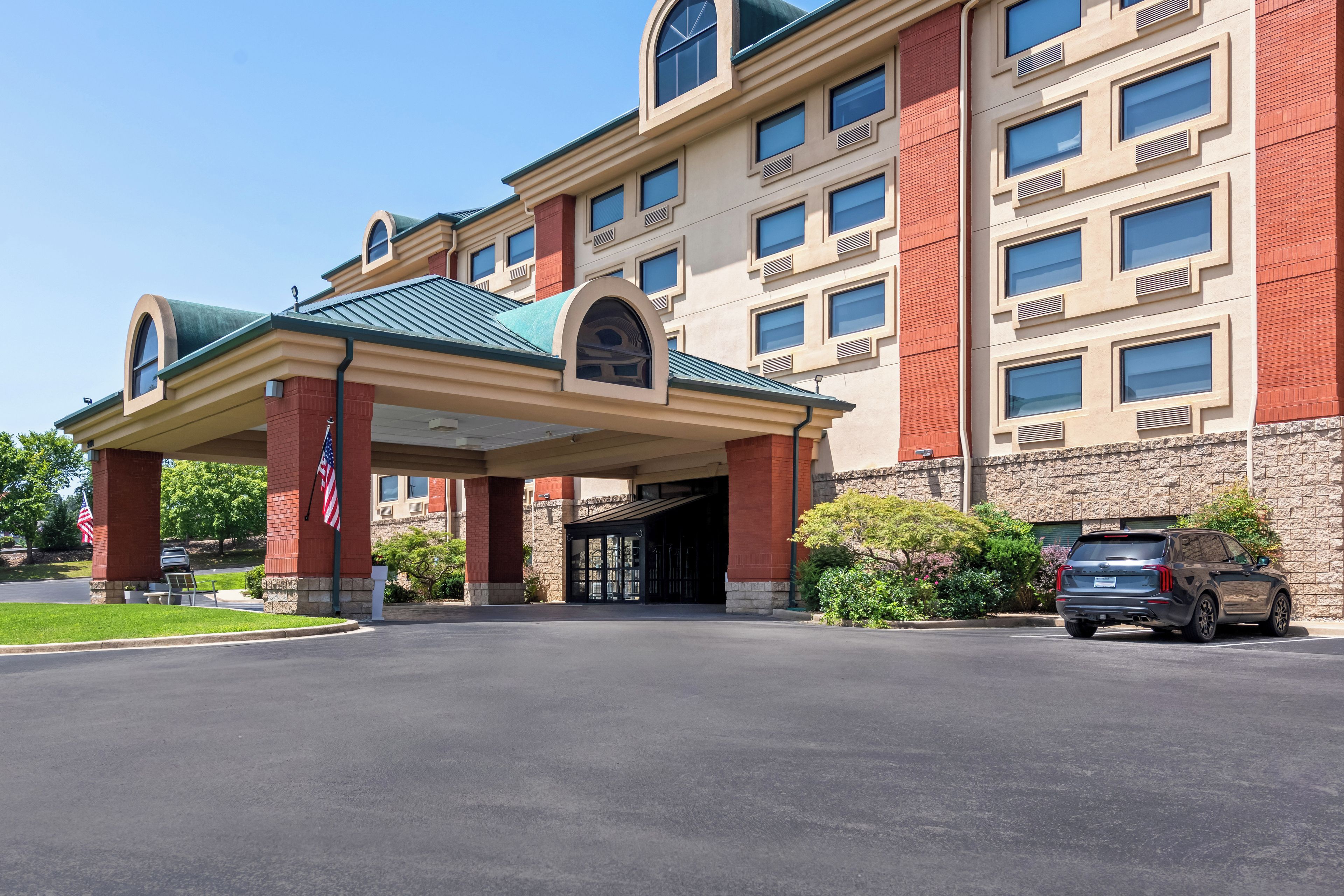 Entrada de hotel con acceso vehicular cubierto, varias ventanas y un SUV estacionado.