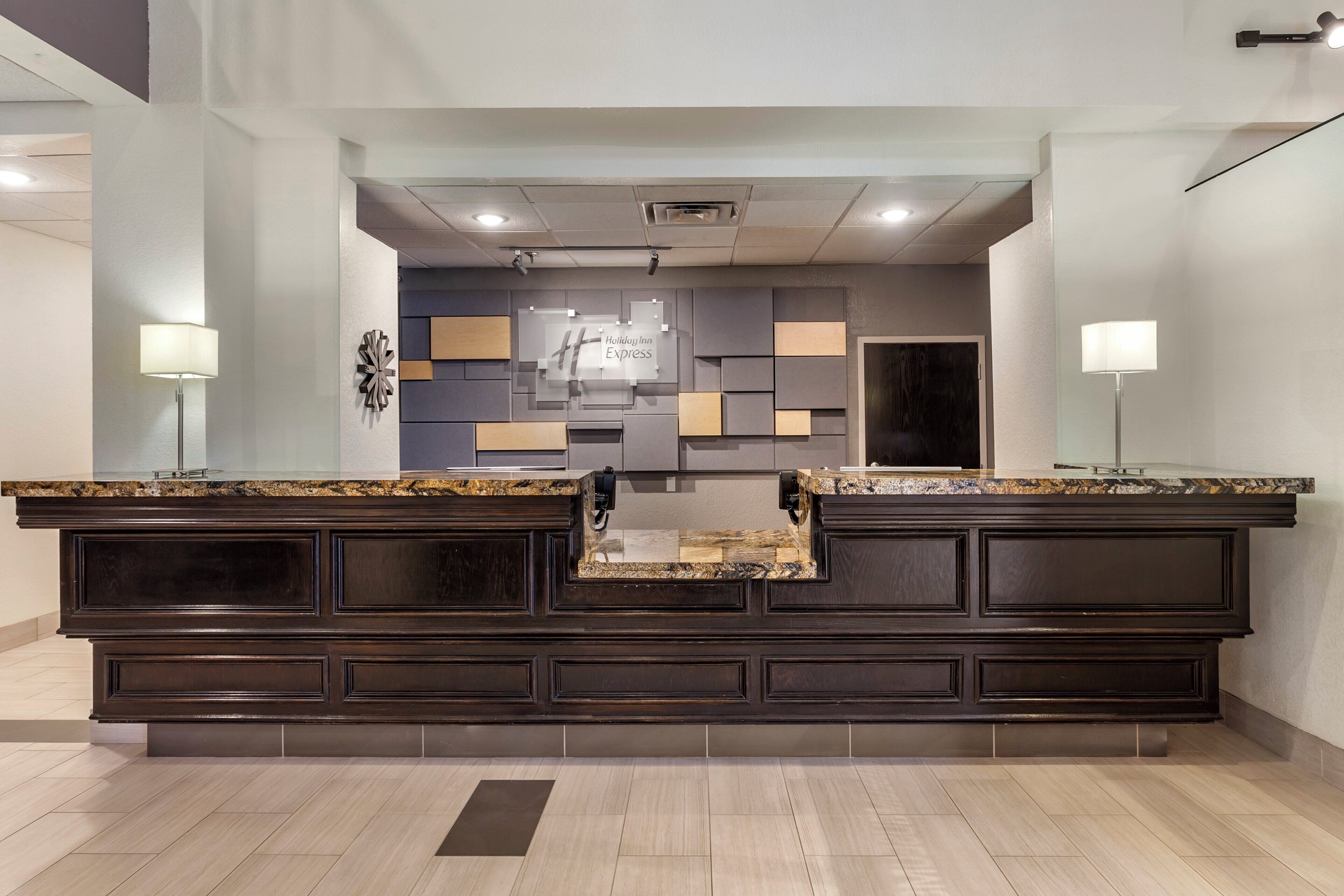A reception area with a dark wood counter, a glass-top desk, and a modern wall design.