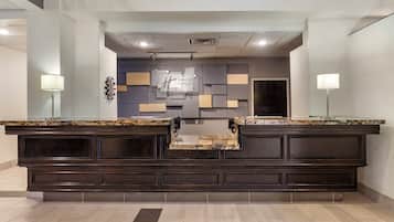 A reception area with a dark wood counter, a glass-top desk, and a modern wall design.
