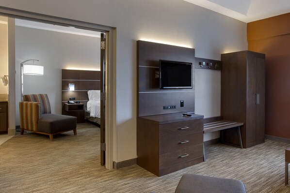 A hotel room with a flat-screen TV mounted on the wall, a desk with drawers, a large wardrobe, a cushioned chair, and a bedside table with a lamp. - Holiday Inn Express Branson-Green Mountain Drive by IHG (Branson)
