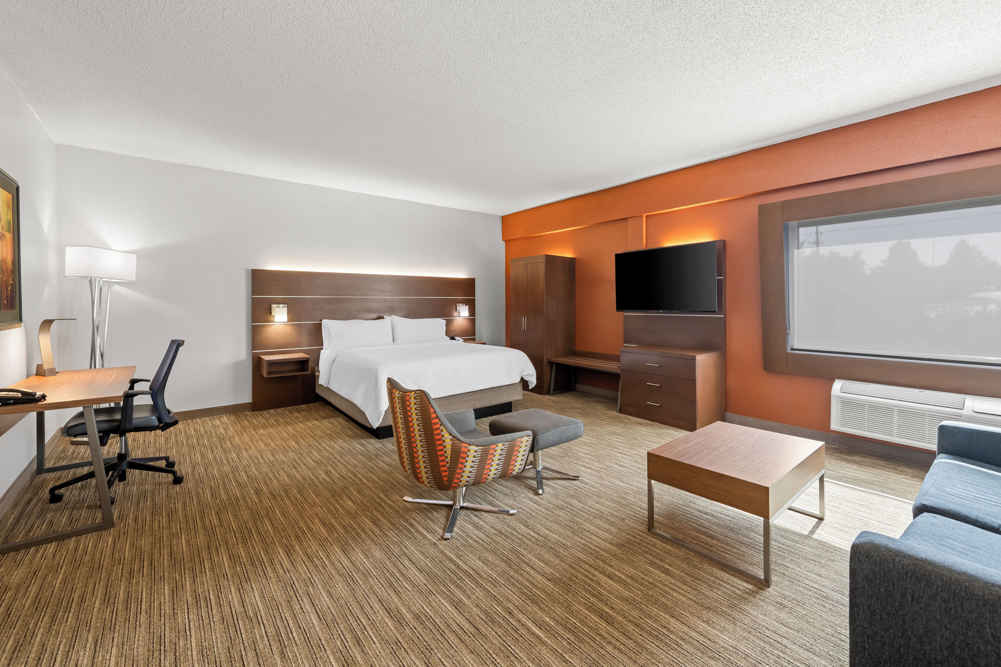 A hotel room with a bed, desk, chair, television, and a large window.