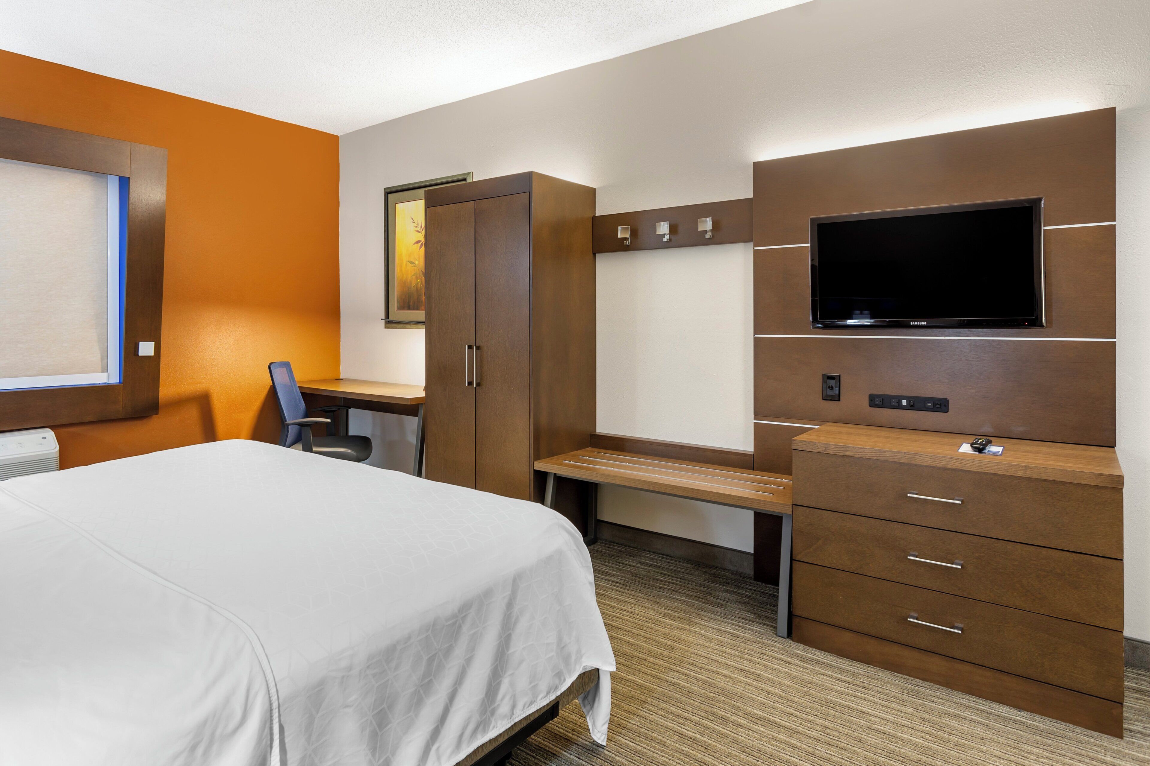 Een hotelkamer met een bed, bureau, stoel, garderobe, televisie en een klein tafeltje.