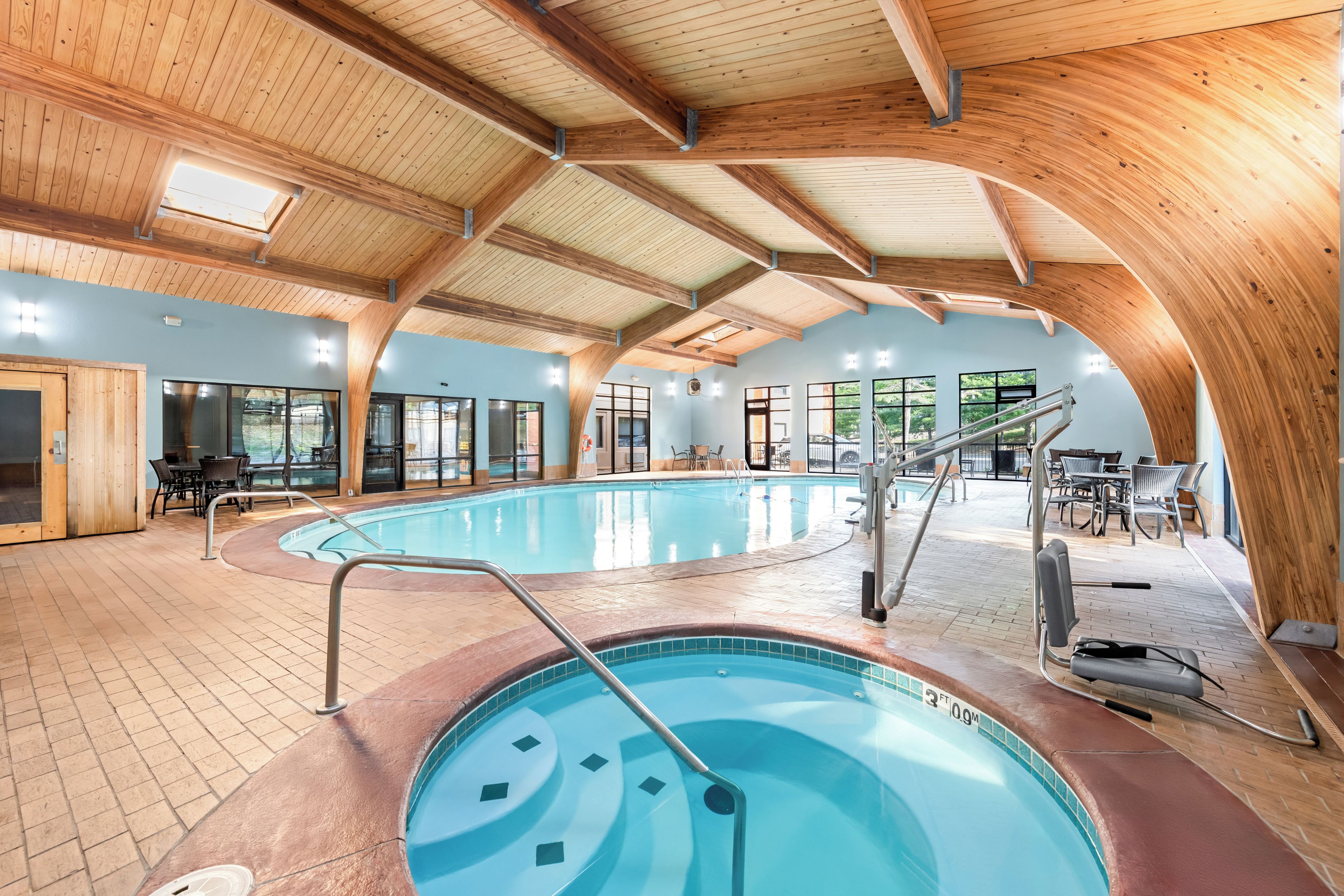 Une piscine intérieure dotée d’un plafond et de murs en bois, entourée d’espaces de détente et de grandes fenêtres.