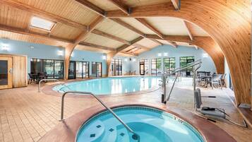 Une piscine intérieure dotée d’un plafond et de murs en bois, entourée d’espaces de détente et de grandes fenêtres.