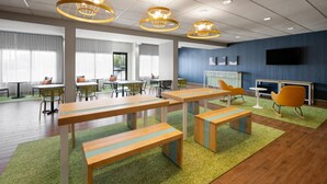 A modern meeting room with tables, chairs, and a television screen.