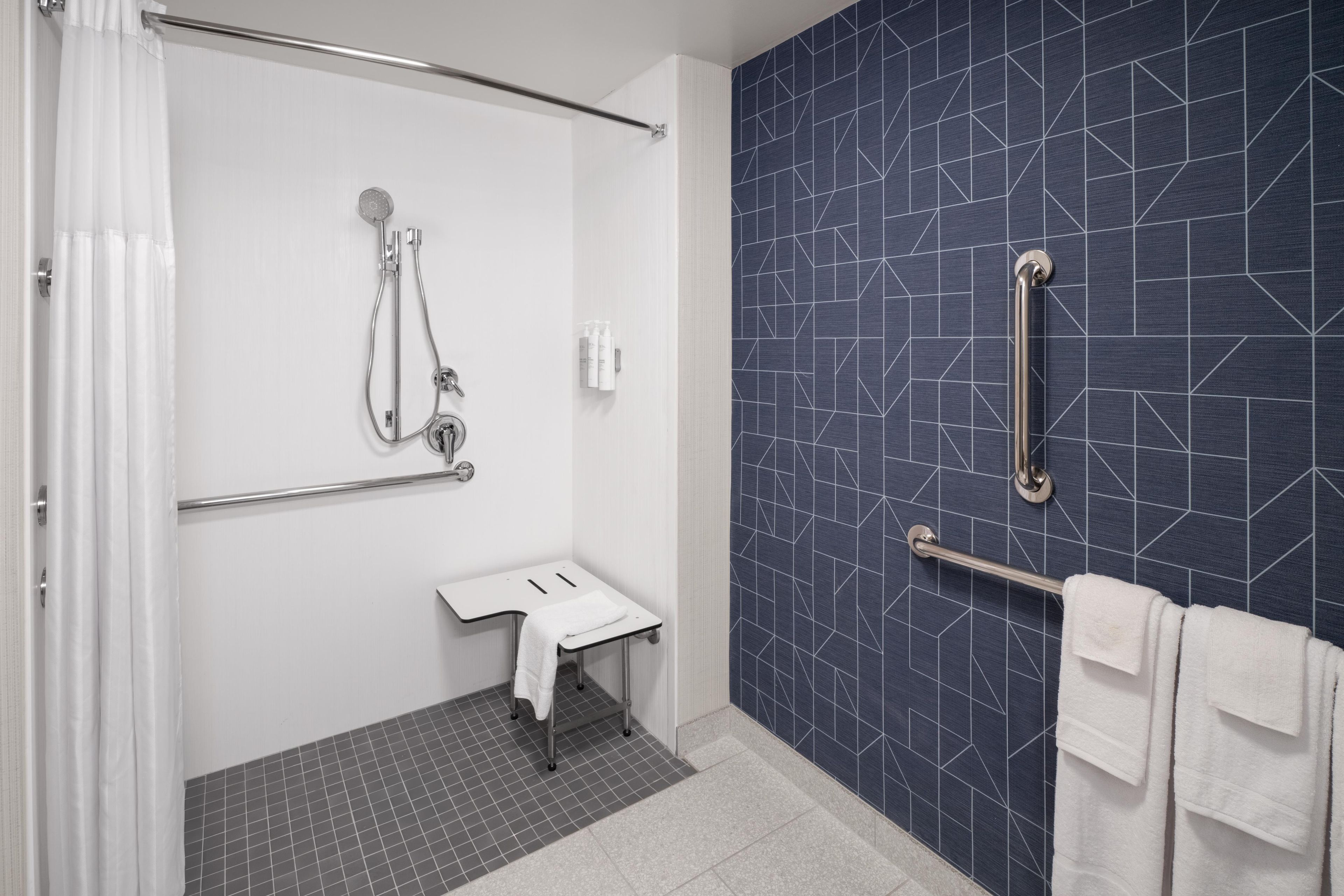 A modern bathroom with a shower, a sink, and a handrail.
