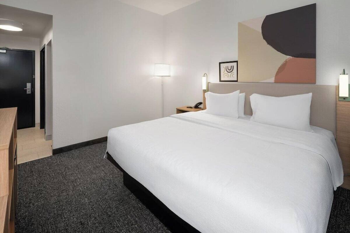 A hotel room with a large bed, a desk, a lamp, and a painting on the wall.