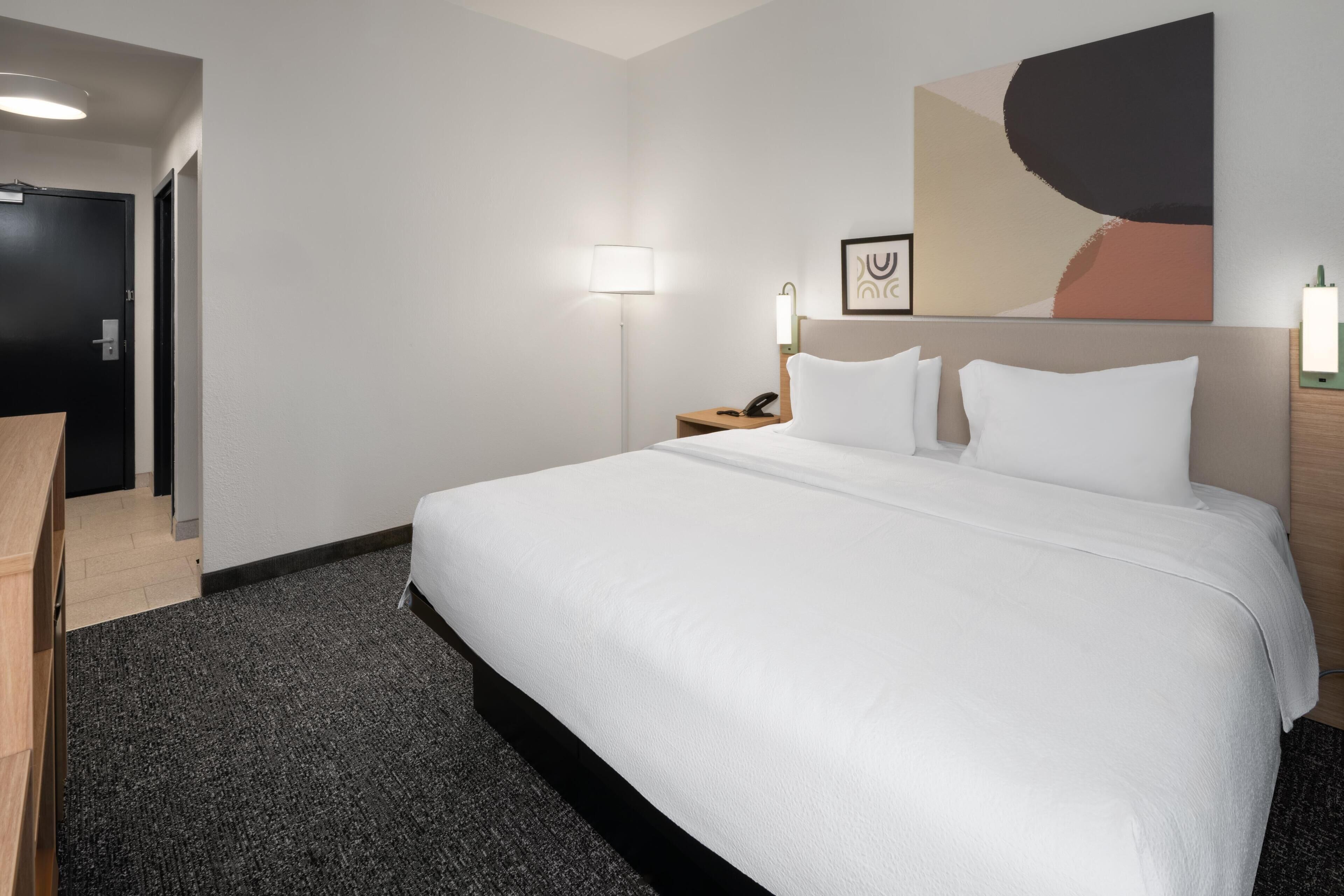 Een hotelkamer met een groot bed, een bureau, een lamp en een schilderij aan de muur.