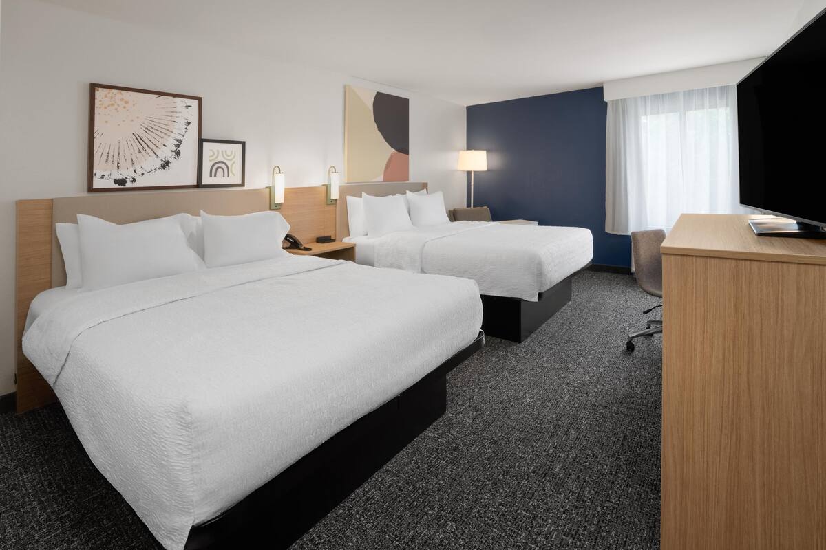 A hotel room with two beds, a desk, a TV, and artwork on the walls.