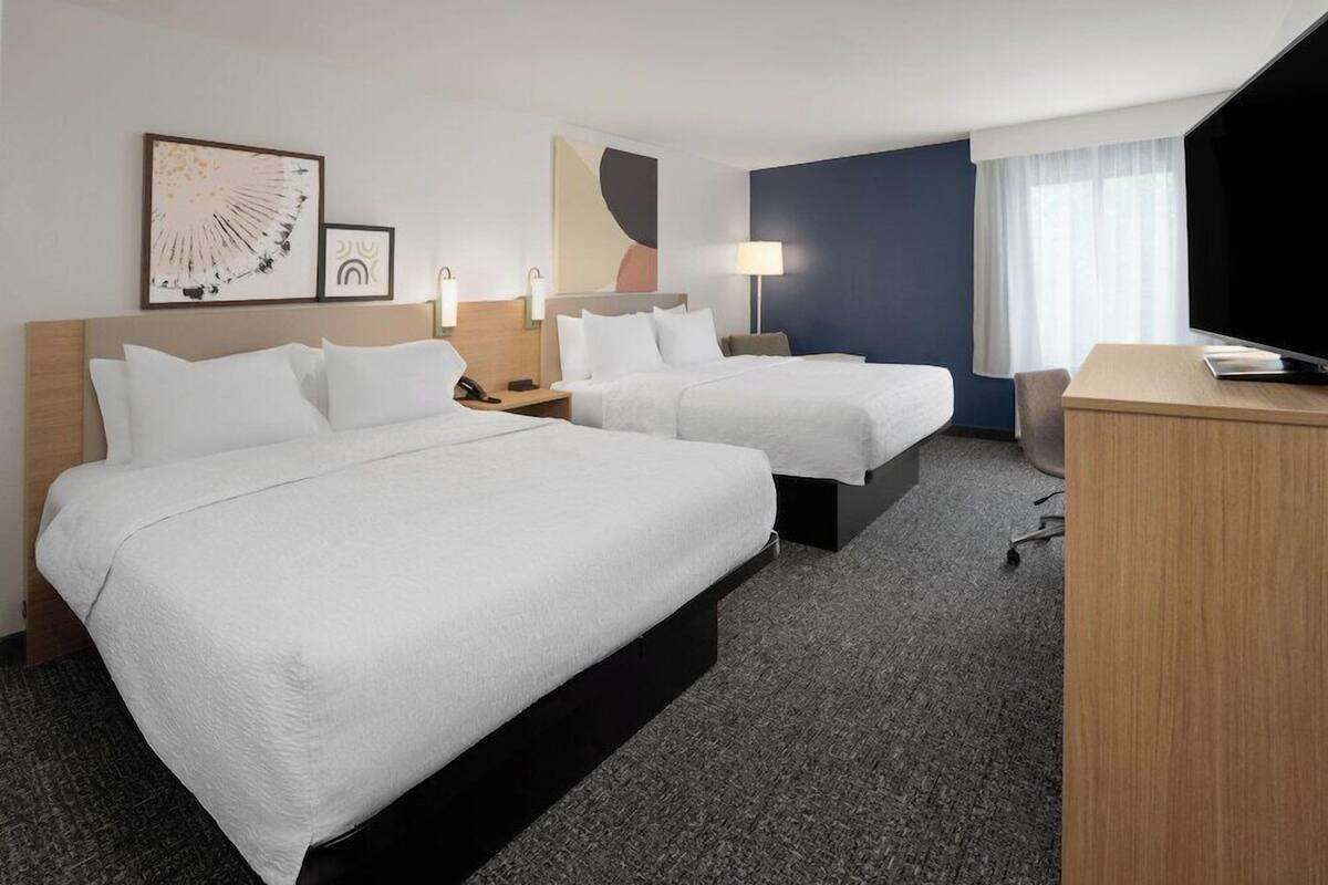 A hotel room with two beds, a desk, a TV, and artwork on the walls.
