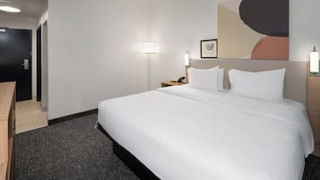 A hotel room with a large bed, a desk, a nightstand with a lamp, and a wall-mounted artwork.