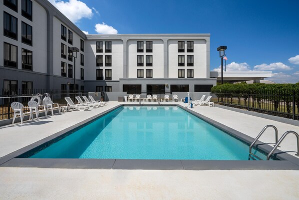 A swimming pool with lounge chairs and a building with multiple windows and balconies.